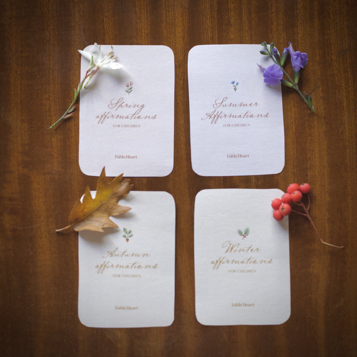 The four seasonal affirmation title cards laid out on a wooden table