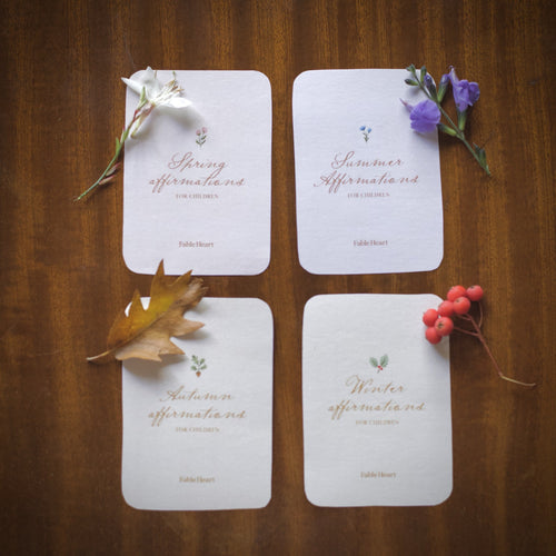 The four seasonal affirmation title cards laid out on a wooden table
